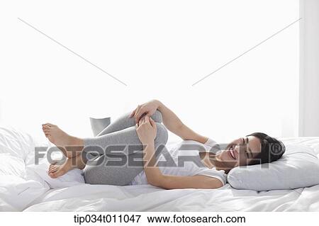 Stock Photo - a woman lying on the bed smiling. Fotosearch
