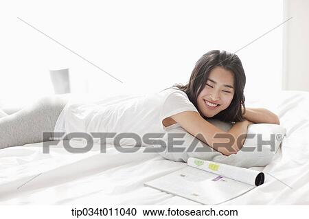 Stock Image - a woman lying on the bed with a magazine next to her. Fotosearch