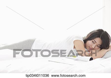 Stock Photograph - a woman lying on the bed with a magazine next to her. Fotosearch