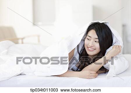 Stock Image - a woman lying on the bed with blanket. Fotosearch