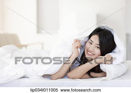 Stock Photography - a woman lying on the bed with blanket. Fotosearch