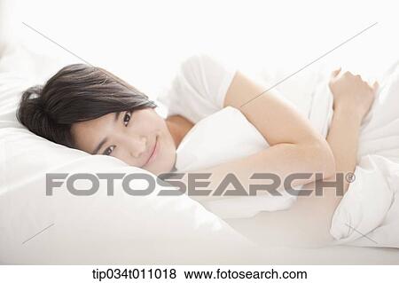 Stock Photo - a woman on the be hugging a pillow. Fotosearch
