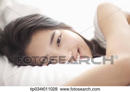 Stock Photo - a woman on the be hugging a pillow. Fotosearch