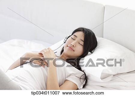 Stock Photo - a woman on the bed listening to music . Fotosearch