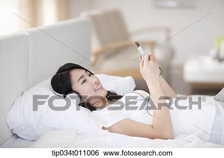 Stock Photograph - a woman on the bed listening to music . Fotosearch
