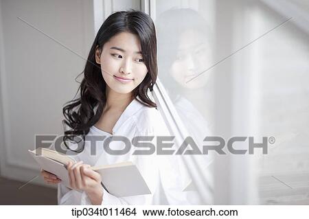 Picture - a woman reading a book leaning on the window. Fotosearch