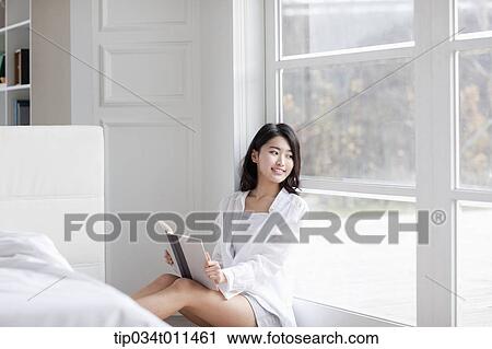 Stock Image - a woman reading a book leaning on the window. Fotosearch