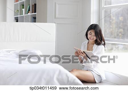 Stock Photo - a woman reading a book leaning on the window. Fotosearch