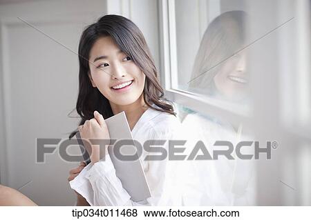 Stock Photo - a woman reading a book leaning on the window. Fotosearch