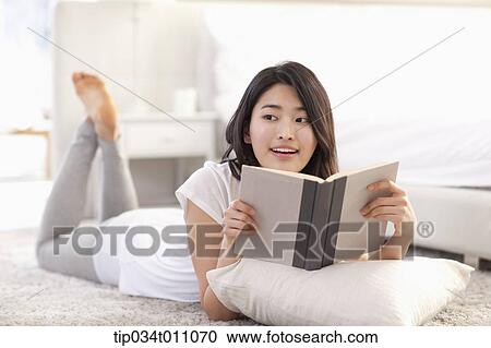 Stock Image - a woman reading a book lying on the floor with a pillow. Fotosearch