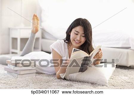 Stock Photo - a woman reading a book lying on the floor with a pillow. Fotosearch
