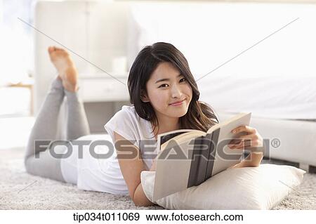 Stock Photo - a woman reading a book lying on the floor with a pillow. Fotosearch
