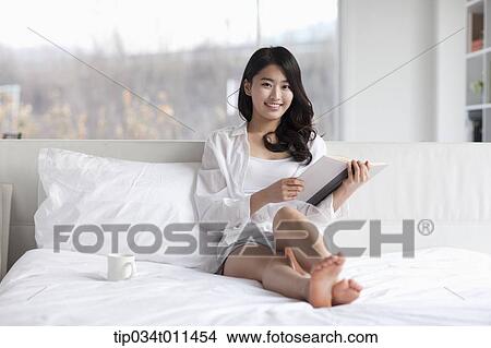 Picture - a woman reading a book on the bed. Fotosearch