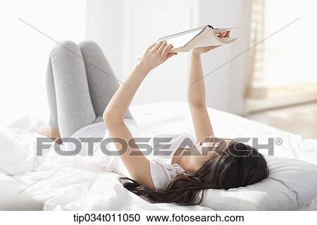 Stock Image - a woman reading a book on the bed. Fotosearch