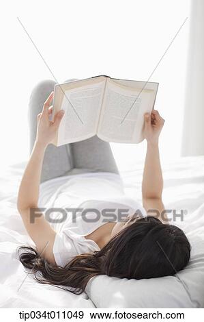 Stock Photo - a woman reading a book on the bed. Fotosearch