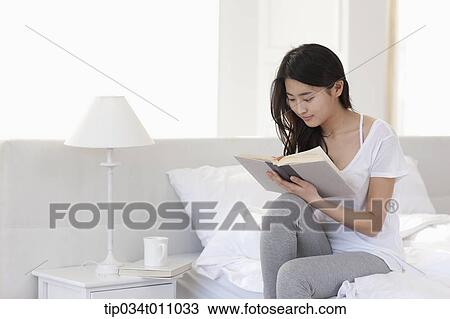 a woman reading a book while sitting on the edge of the bed View Large Photo Image Stock Image - a woman reading a book while sitting on the edge of the bed. Fotosearch