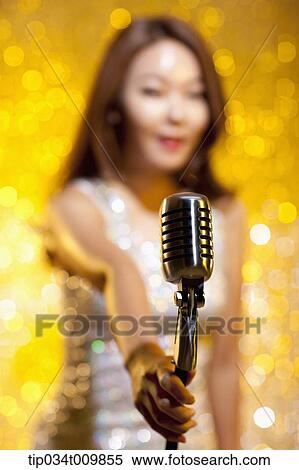 Stock Photography - a woman singing with microphone in fancy dress in sparkling background. Fotosearch