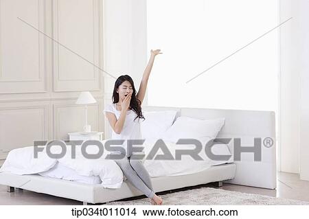 Picture - a woman sitting on the bed after sleep. Fotosearch