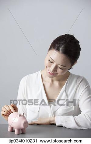 Stock Image - a woman smiling at desk with a piggy bank . Fotosearch