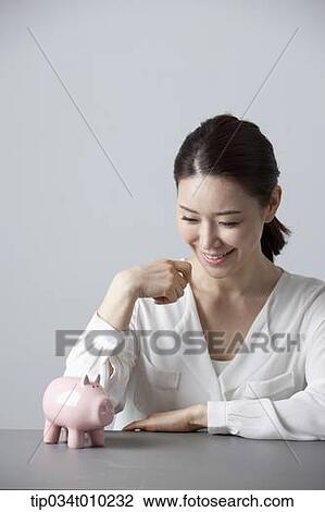 Stock Image - a woman smiling at desk with a piggy bank . Fotosearch