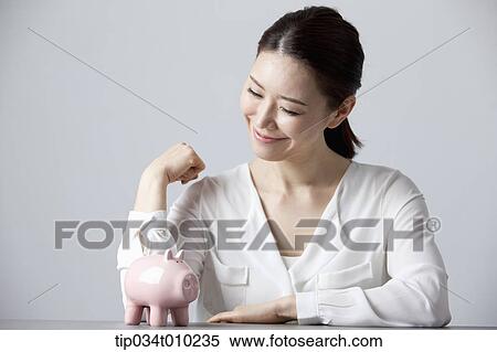 Stock Photography - a woman smiling at desk with a piggy bank . Fotosearch