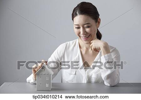 Picture - a woman smiling at desk with a small house block. Fotosearch