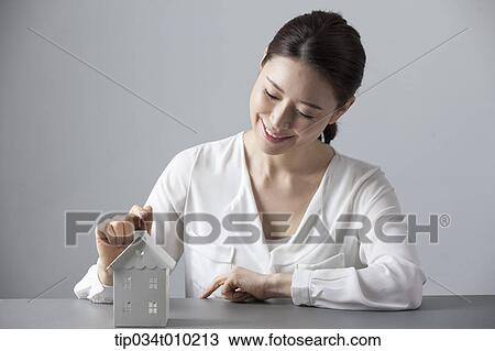 Stock Image - a woman smiling at desk with a small house block. Fotosearch