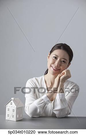 Stock Image - a woman smiling at desk with a small house block. Fotosearch