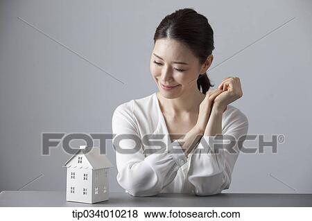 Stock Photo - a woman smiling at desk with a small house block. Fotosearch