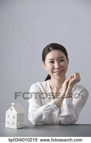 Stock Photo - a woman smiling at desk with a small house block. Fotosearch