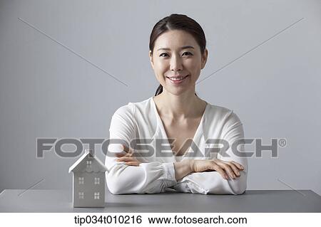 Stock Photograph - a woman smiling at desk with a small house block. Fotosearch