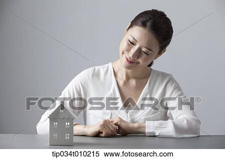 Stock Photography - a woman smiling at desk with a small house block. Fotosearch