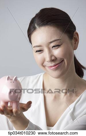 Stock Image - a woman smiling while holding a piggy bank. Fotosearch