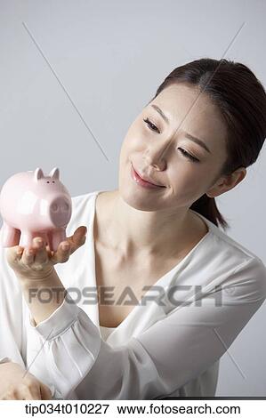 Stock Photo - a woman smiling while holding a piggy bank. Fotosearch