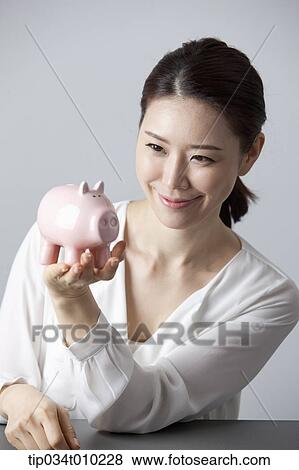 Stock Photo - a woman smiling while holding a piggy bank. Fotosearch
