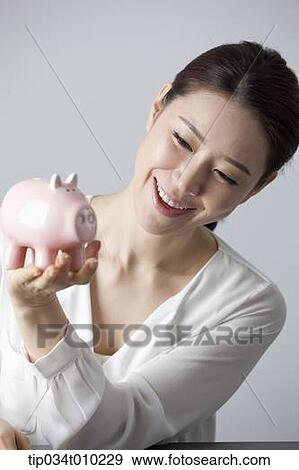 Stock Photo - a woman smiling while holding a piggy bank. Fotosearch