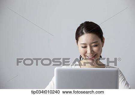 Stock Image - a woman smiling while using a laptop. Fotosearch