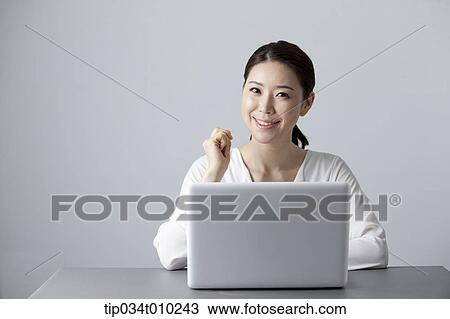 Stock Image - a woman smiling while using a laptop. Fotosearch