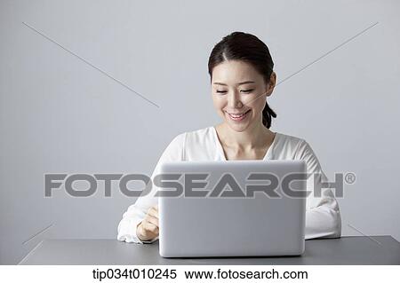 a woman smiling while using a laptop View Large Photo Image Stock Photography - a woman smiling while using a laptop. Fotosearch