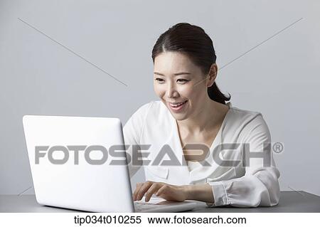 Stock Photography - a woman smiling while using a laptop. Fotosearch