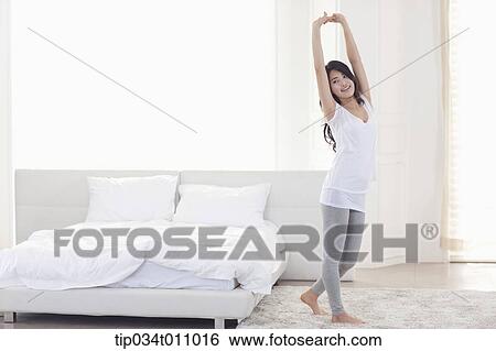Stock Photograph - a woman stretching next to a bed. Fotosearch