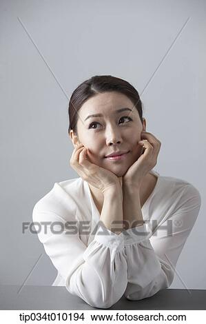 Picture - a woman thinking while sitting at a desk. Fotosearch