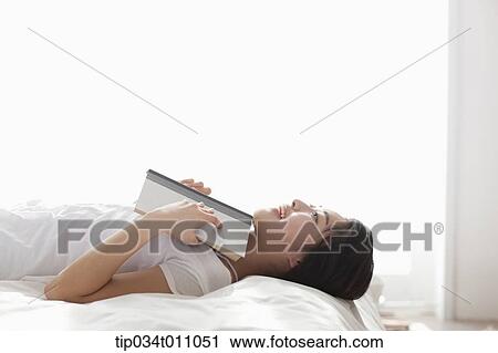 Stock Image - a woman with a book on the bed. Fotosearch