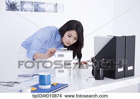 Picture - an interior designer at her desk with a model house. Fotosearch