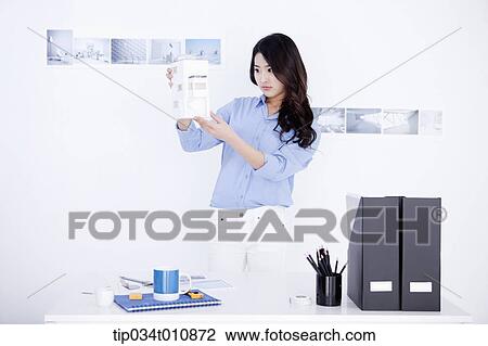 Stock Image - an interior designer at her desk with a model house. Fotosearch