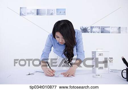 Stock Photo - an interior designer at her desk with a model house. Fotosearch