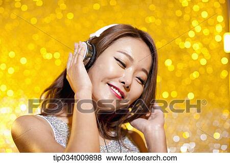 Stock Photo - close up of a woman in fancy dress listening to music with headphone. Fotosearch