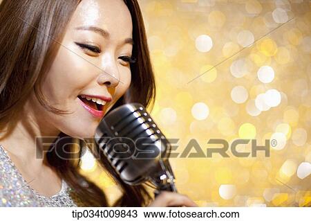 Stock Image - close up of a woman singing with microphone in fancy dress. Fotosearch