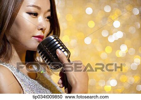 Stock Image - close up of a woman singing with microphone in fancy dress. Fotosearch
