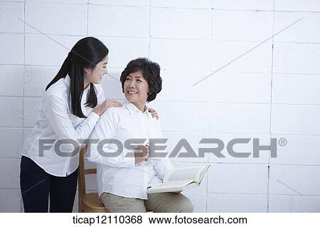 Stock Photo - daughter next to mother reading a book. Fotosearch